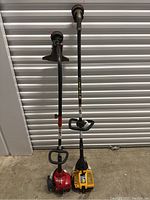 Wide angle shot showing two gas-powered weed whackers side by side with straight shafts, engines at base, handles and trimming heads.