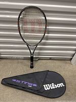 Full view of Wilson Sting Comp tennis racquet standing vertically with its cover beside it.