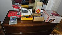 Wide view showing all items on wooden table including cameras, massager, heat pack box, and fan