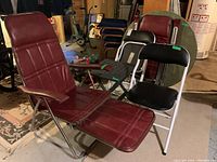Two mid-century modern burgundy padded vinyl chairs with pull out footrests, two black folding chairs with metal frames behind, basement setting