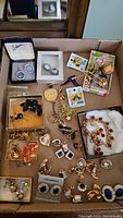 Full view of multiple vintage costume jewelry pieces in a box including earrings, brooches, and pins with some in their original packaging.