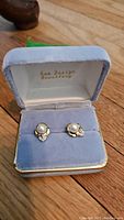 Front view of gold pearl earrings displayed side by side in a grey velvet jewelry box