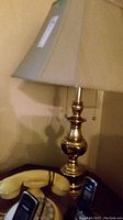 One lamp showing polished brass base with beige shade and pull chain switch. Yellow rotary phone and cordless phones visible at base.