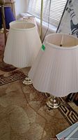 Pair of matching table lamps with white pleated fabric shades on a patterned carpet.