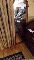 Full view of the wall mirror showing the wooden frame with an arched top, placed near curtains and furniture.