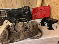 Four designer purses: two black Michael Kors purses with gold chain and MK charm, one red Ralph Lauren purse with embossed RL logo and tassel detail, and one snake print purse.