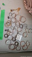 A collection of various silver hoop earrings, silver rings, and a colorful gold-plated pendant laid out on fabric.