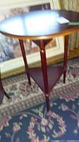 Full view of round top wooden drop leaf table with three straight legs and triangular lower shelf, showing style and condition.