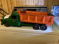 Side view of vintage Structo dump truck showing green cab and orange dump bed with some wear and rust.