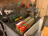Overview of the train set components arranged on a table, including the two tall metal towers with signal lights, several Santa Fe metal rail cars in red and yellow paint, and parts of the track set.