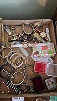 Full view of assorted watches, bracelets, bangles, ring boxes, and a pouch in a cardboard box