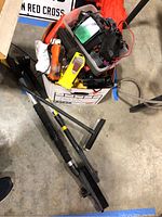 Photo shows a box of assorted flashlights, headlamp, and ice scrapers with automotive brushes on a concrete floor.