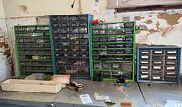 Wide view of five metal-framed multi-drawer storage organizers on a workbench, some drawers missing or open, labeled with handwritten tags