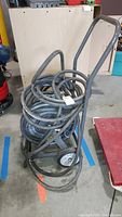 Front view of black garden hose coiled on gray metal reel with wheels and handle.