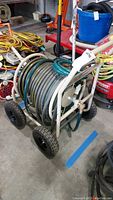Front and side angle showing metal hose reel mounted on a four-wheel frame with handle and wound hose.