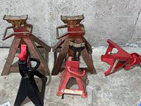 Five metal jack stands including large, medium, and small red weathered stands and one black Craftsman jack stand, showing the entire lot arrangement.