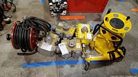 Overview of the lot showing four junction blocks, yellow cord reel, and yellow work light all arranged on floor with colored tape lines