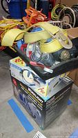 Yellow and blue ratchet straps with metal hooks piled on a black tray above the boxed Regent worklight in a garage setting.