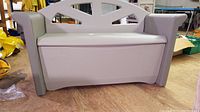Front view of beige and gray Rubbermaid outdoor storage bench with backrest and armrests, showing closed lid.