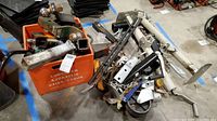 Wide view showing an orange storage bin filled with hitch balls, ball mounts, and metal parts next to scattered hitch tubes and brackets on the floor.
