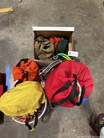 Lot of climbing gear including fabric bags of different colors containing ropes and hardware, carabiners, and pulleys, all placed on concrete floor.