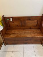 Front view of wooden hallway bench showing paneled backrest, hinged seat, and curved armrests with visible surface scratches.