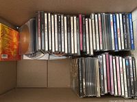 Box containing multiple music CDs in jewel cases. Various genres and artists including classic rock and pop.