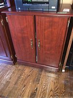 Front view of cabinet showing reddish wood finish, brass handles, and panel doors.