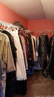 View of clothes hanging on white metal racks including jackets, shirts, and dresses in an orange-walled room.