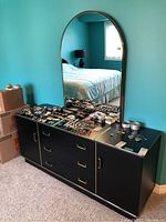 Full view of black dresser with large arched mirror on top, showing multiple jewelry items placed on surface