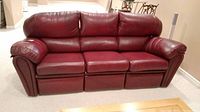 Front view of three-seat burgundy leather sofa in basement room, all seats in upright position
