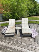 Two metal-frame lounge chairs with padded cushions and a small white plastic side table on a wooden deck, with fabric covers laid aside.