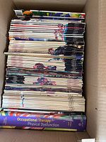 Top-down view of Nintendo Power magazines and Occupational Therapy textbook in cardboard box