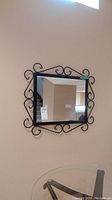 Wall-mounted square mirror with black metal frame and scrollwork design, clear reflective surface.