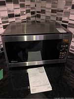 Full view of Panasonic microwave oven with manual on black granite counter and tiled backsplash.