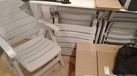 Four light gray plastic folding patio chairs stacked and one opened, stored in basement area.