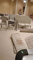 Photo shows stacked beige plastic chairs, folded patio table parts including legs and support bars, cushions stacked on floor, and an end table on side.