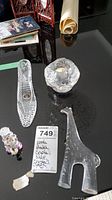 Top-down view of all four items: crystal shoe, glass candle holder, crystal giraffe with repaired neck, and colorful clown figurine on black table.