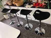 Four black saddle-style barstools in a kitchen setting, showing overall condition and design.
