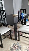 Black lacquer finished dining table surface with some items on the table and surrounding four black chairs with light-colored cushioned seats.