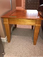 Side angle showing light wood veneer side table with tapered legs and carved horizontal groove details near the top.