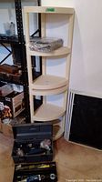 Beige plastic corner shelf with five shelves, plastic toolbox open showing various tools inside, including a Mastercraft drill and other hand tools. Window screens visible nearby not included.