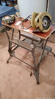 Front view of folding work bench with jigsaw and circular saw placed on top, showing metal frame and plywood surface.