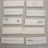 Top view of all 10 stylus pen boxes arranged flat, showing various branded and plain white packaging with printed pen outlines and product details.