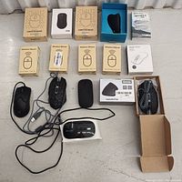 Top-down view of all 15 computer mice, both loose and boxed, with USB cables tangled mostly black in color.