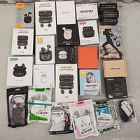 All 27 wireless earbuds and accessories laid out together on a table. Various packaging styles and colors visible, showing brand names and images of earbuds.