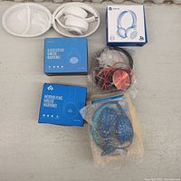 Overview of 6 headphones including boxes and some headphones in protective packaging and carrying case.