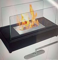 Ethanol fireplace model SP-017TJ in use with visible open flame and clear glass panels on black fireplace body.