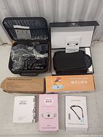 Overall view of lot showing massage gun set with attachments and charger, heating massage belt with user guide, boxed neck massager, auto heating pad, and rechargeable LED neck reading light box.