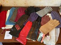 Photo of 14 pairs of ladies leather gloves in various colors and styles arranged on a wooden surface.